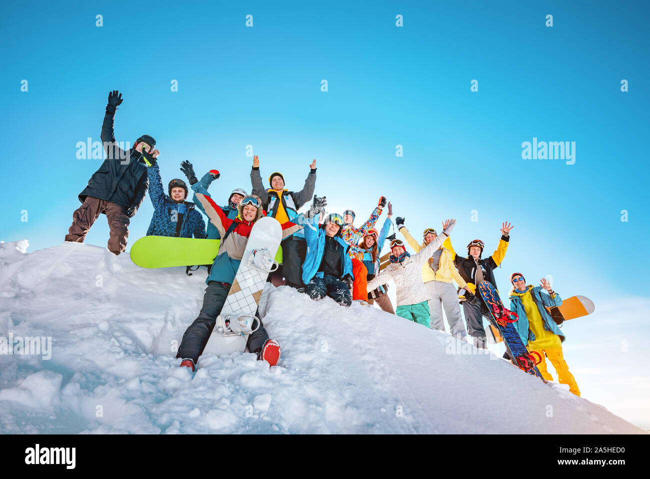 Big group of happy skiers and snowboarders with raised arms stands on snowdrift at ski resort. Ski and snowboard concept Stock Photo