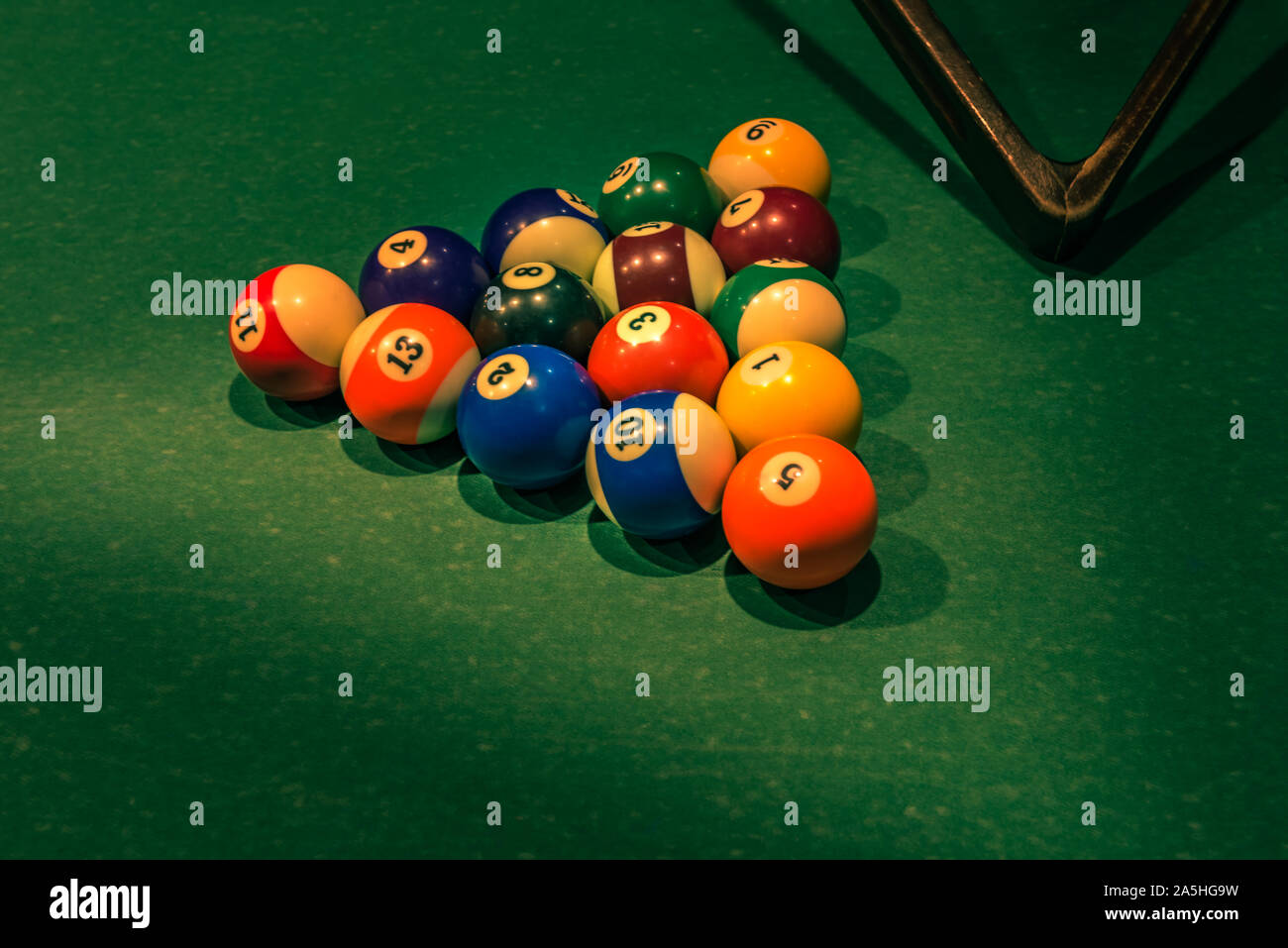 Set of colorful numbered balls on green table and partly visible wooden triangle. Horizontal background with equipment for Americal billiard cue sport Stock Photo