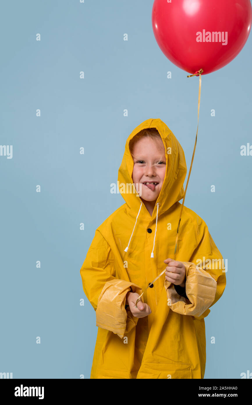 Little boy in yellow raincoat with red balloon over blue background Stock  Photo - Alamy