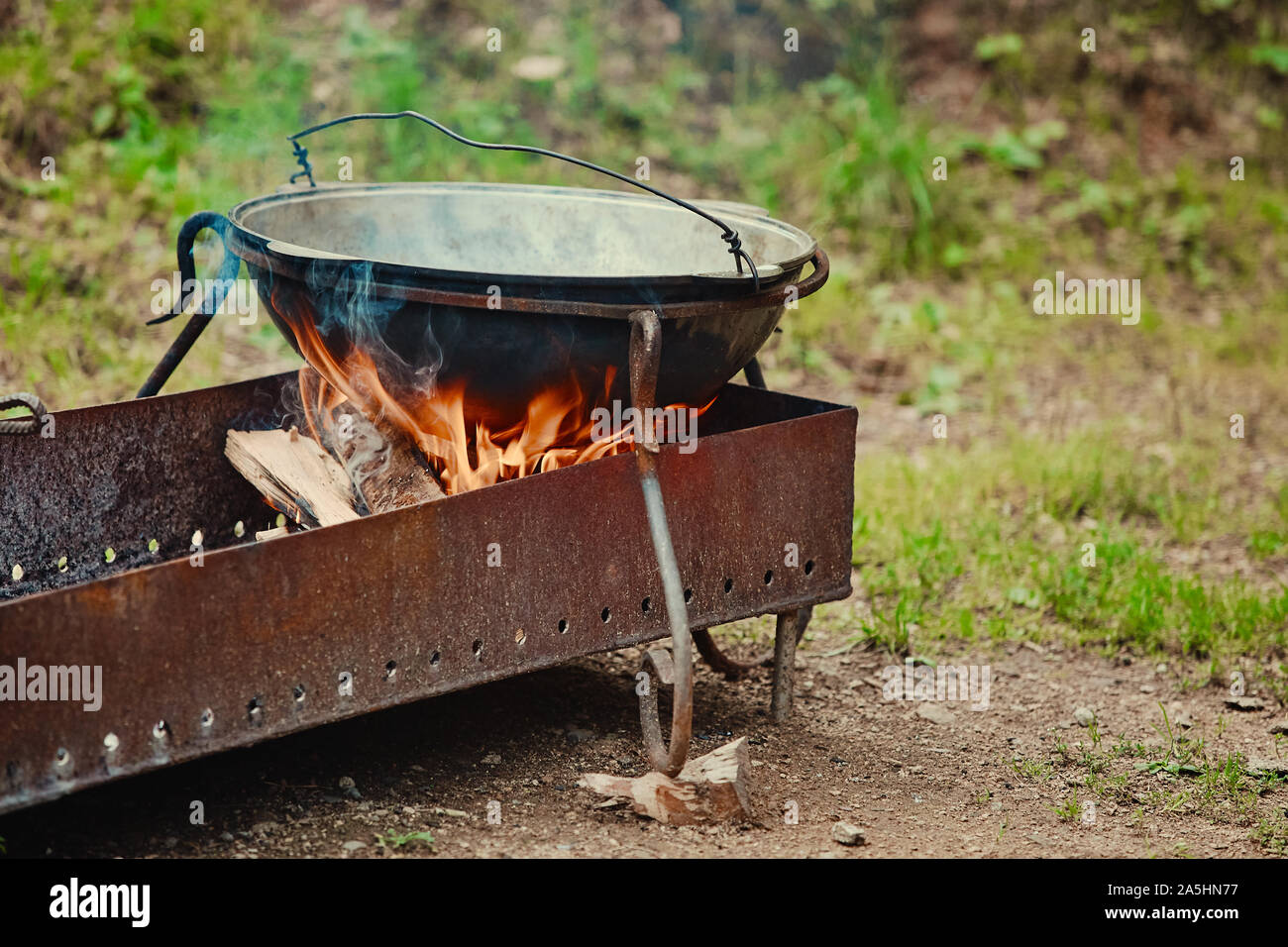 A metal boiler stands on a grill with fire and firewood, in a tourist  Parking lot Stock Photo - Alamy