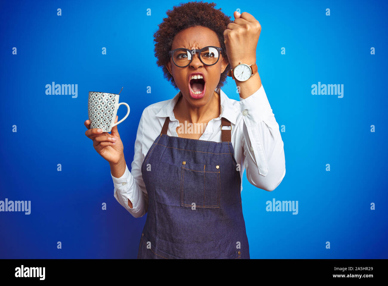 African american barista woman wearing bartender uniform holding cup over blue background annoyed and frustrated shouting with anger, crazy and yellin Stock Photo