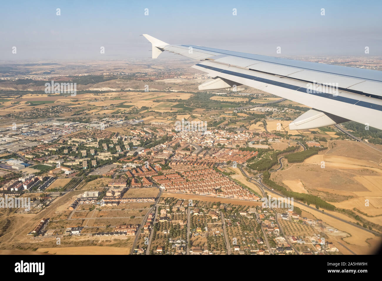 Looking through aircraft window during flight. Aircraft wing over blue skies and cityscape  .Copy space. Stock Photo