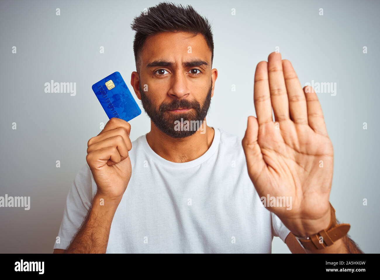 Young indian customer man holding credit card standing over isolated ...