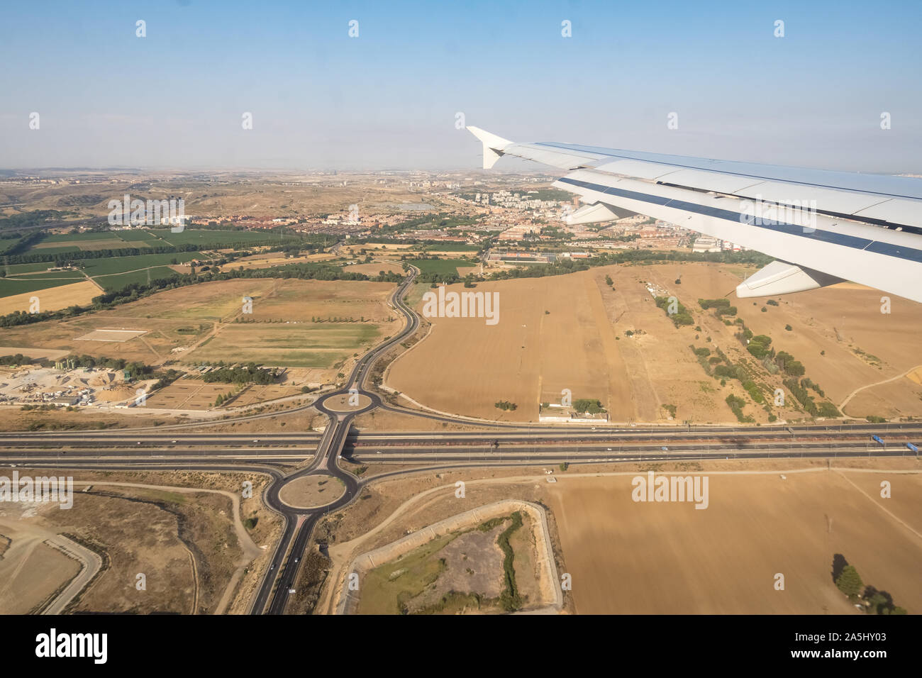 Looking through aircraft window during flight. Aircraft wing over blue skies,crossroad and cityscape background .Copy space. Stock Photo