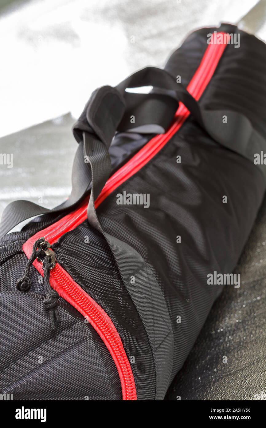 Black photographic tripod case with spectacular red zipper.Selective focus with shallow depth of field. Stock Photo