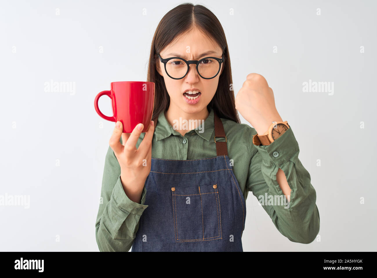 Chinese barista woman wearing apron glasses drinking coffee over isolated white background annoyed and frustrated shouting with anger, crazy and yelli Stock Photo