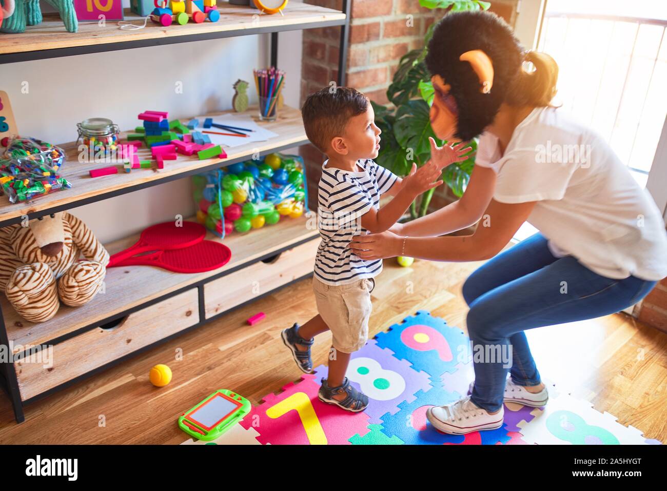 Beautiful teacher and toddler boy playing, woman with monkey mask at kindergarten Stock Photo