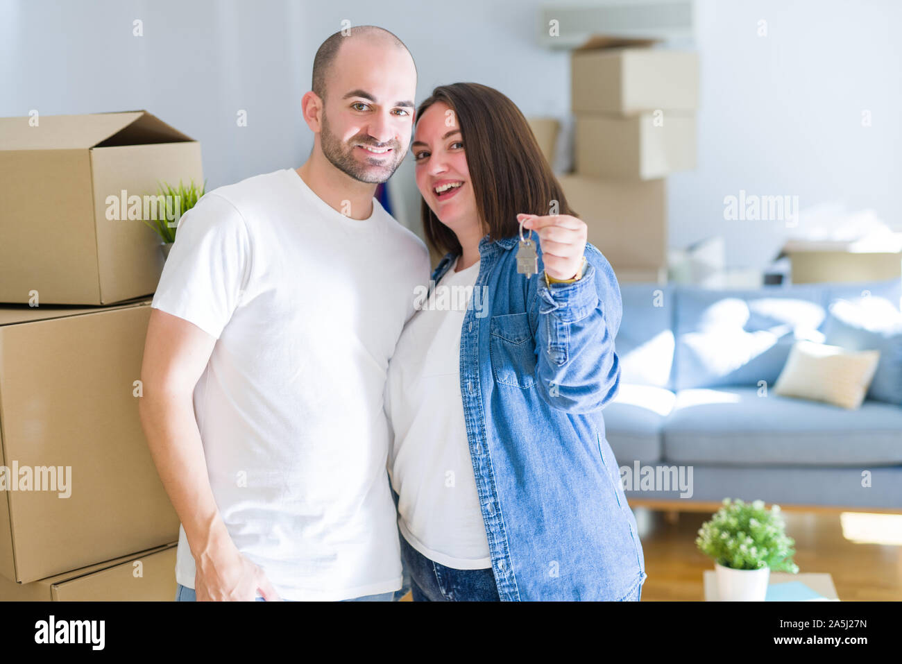 Young couple smiling very happy showing keys of new home, moving and ...