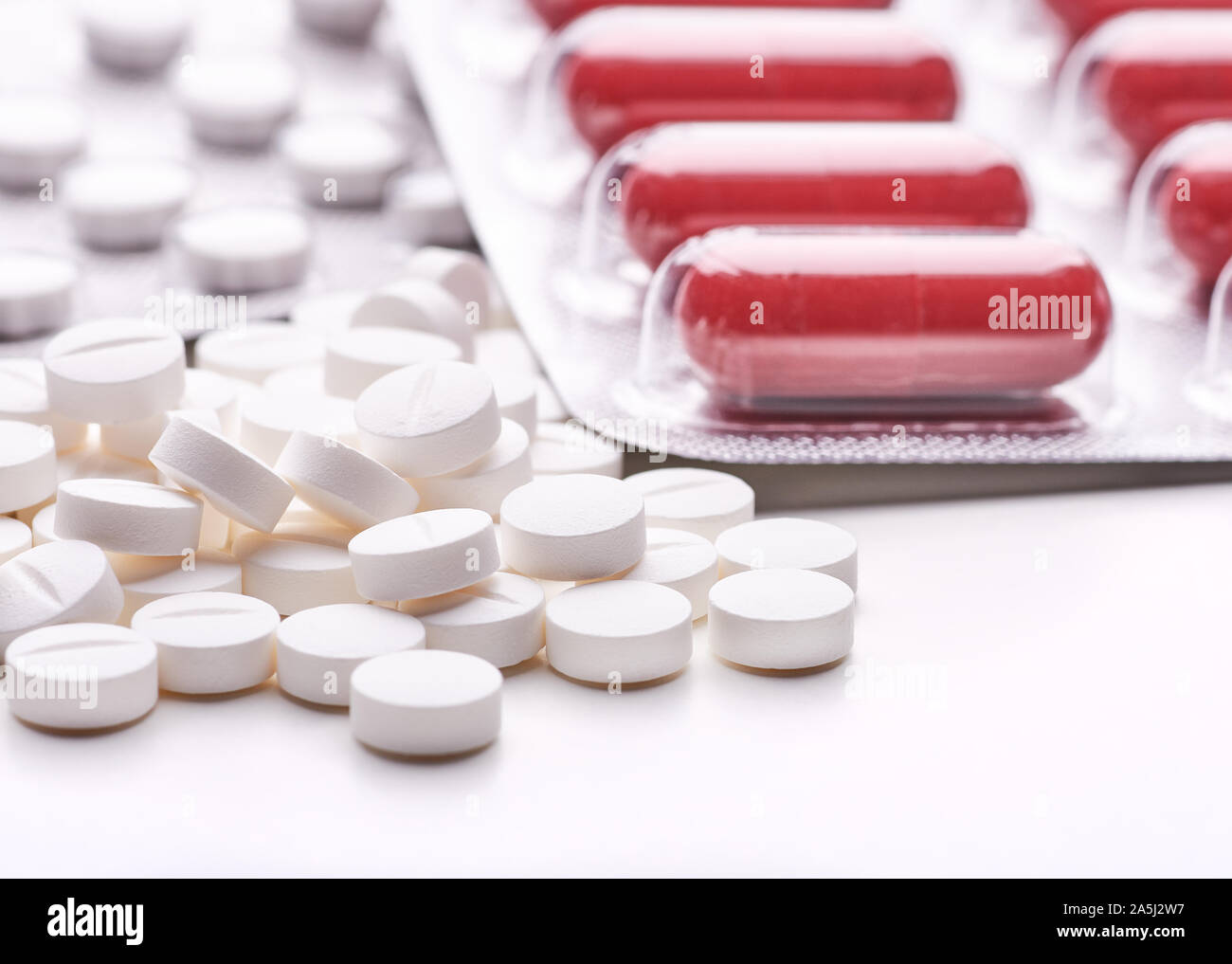 Still life with pile of round pills or tablets, antidepressants or painkillers with space for text. Red capsules in blister pack on white table top. Stock Photo