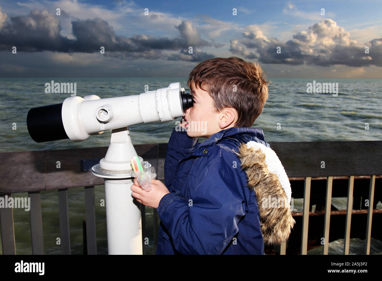 Young child looking through public binoculars on Hastings pier in daytime Stock Photo