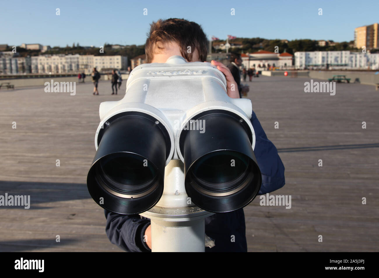 Young child looking through public binoculars on Hastings pier in daytime Stock Photo