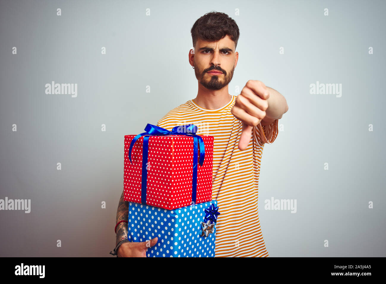 Young man with tattoo holding birthday gifts standing over isolated ...