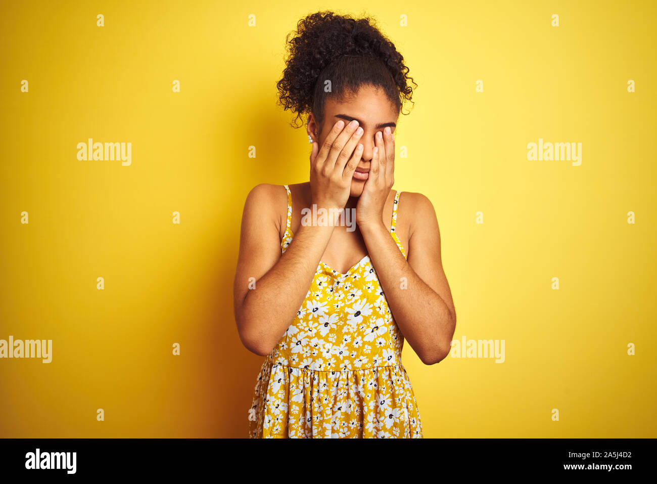 African american woman wearing casual floral dress standing over isolated yellow background rubbing eyes for fatigue and headache, sleepy and tired ex Stock Photo