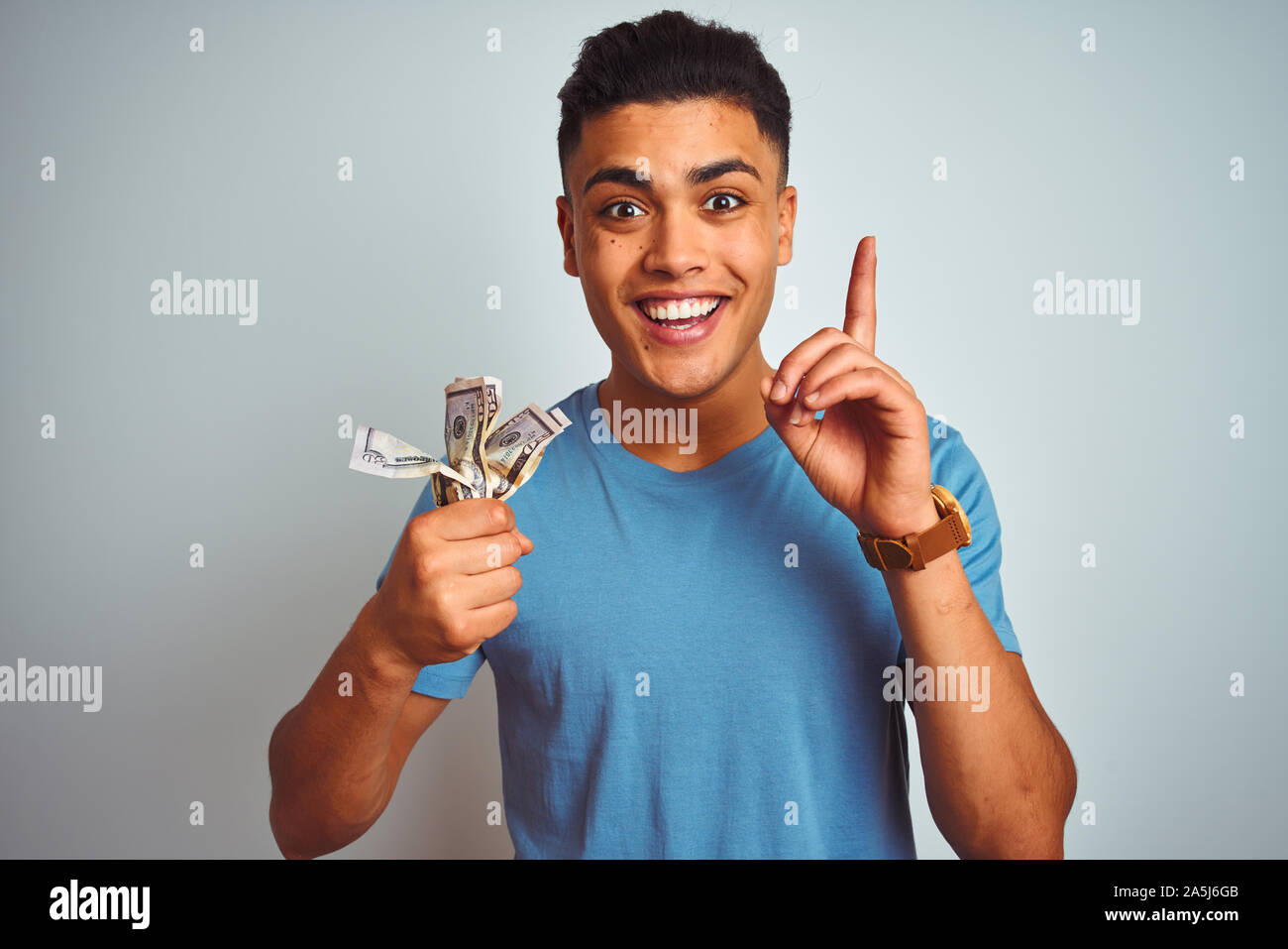 Young brazilian man holding dollars standing over isolated white ...