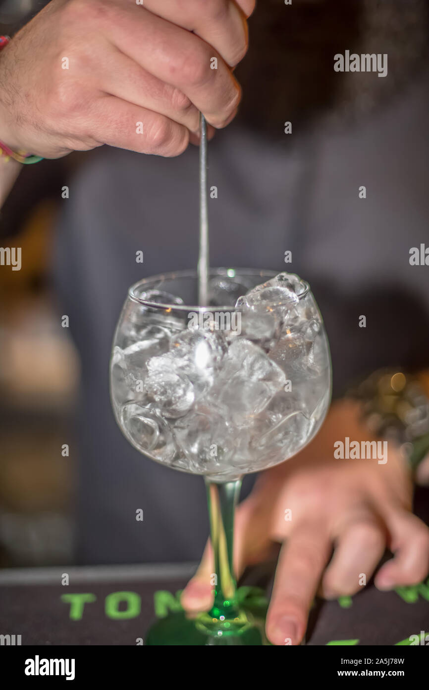 View of bartender preparing glass of tonic gin in flask with lots of ice in bar of drinks, blurred person as background Stock Photo