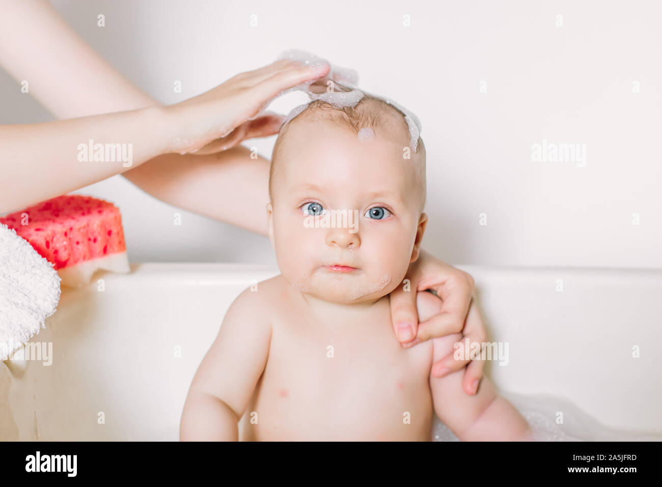 Happy laughing baby taking a bath playing with foam bubbles. Little