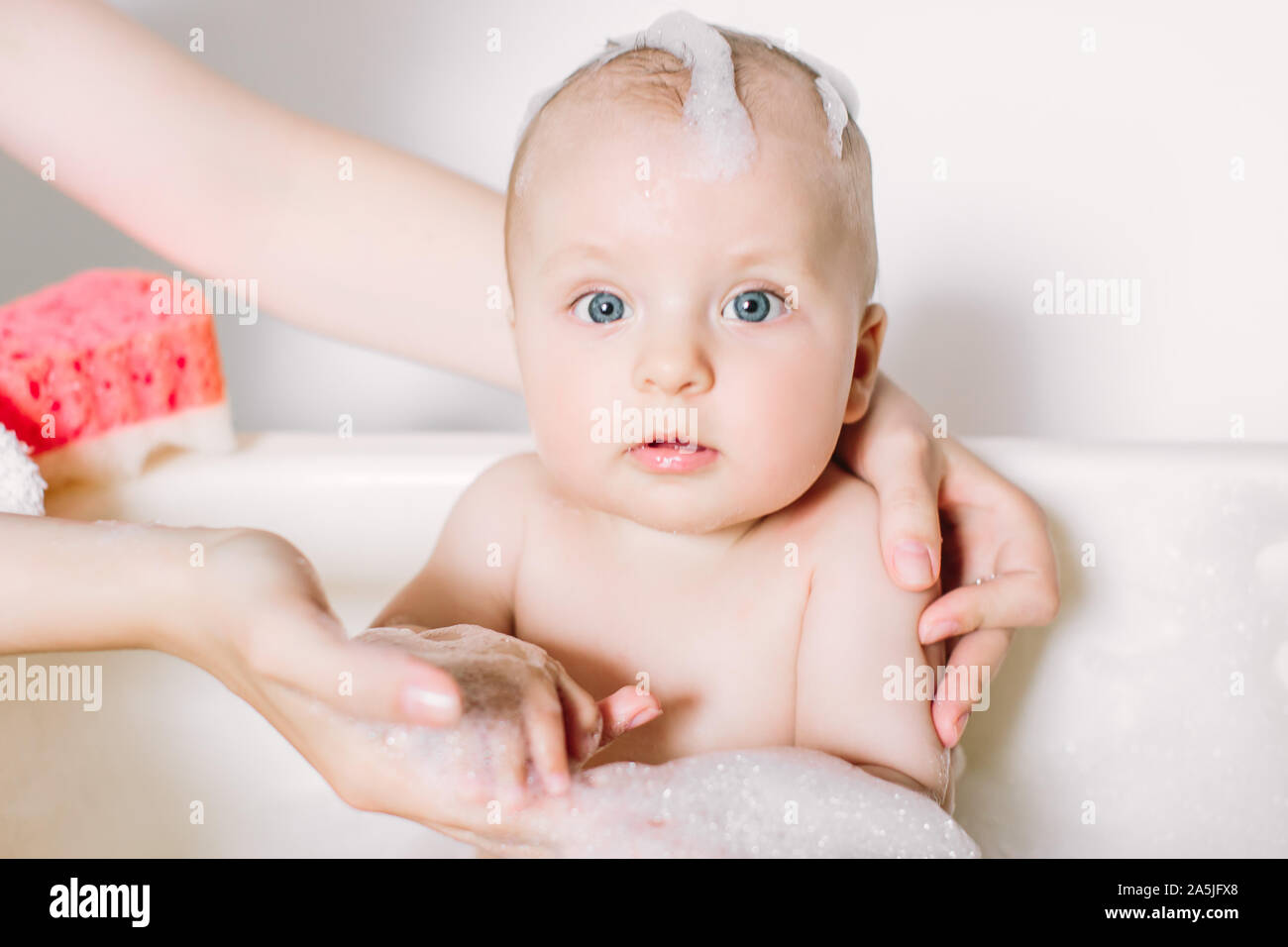 Happy laughing baby taking a bath playing with foam bubbles. Little