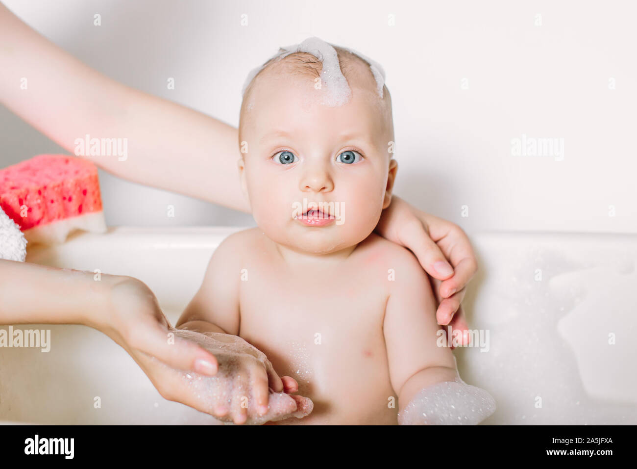 Happy laughing baby taking a bath playing with foam bubbles. Little