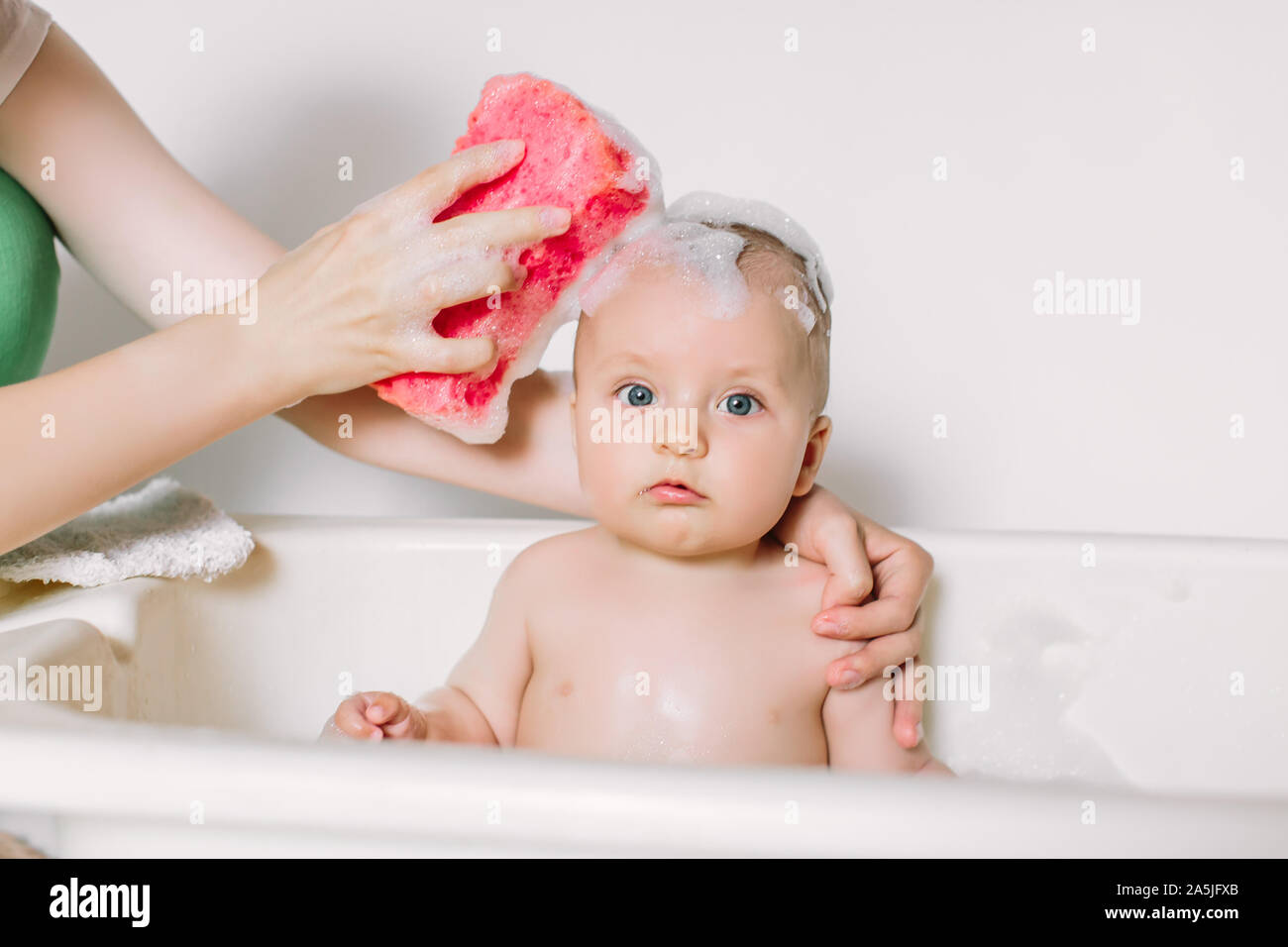 Happy laughing baby taking a bath playing with foam bubbles. Little