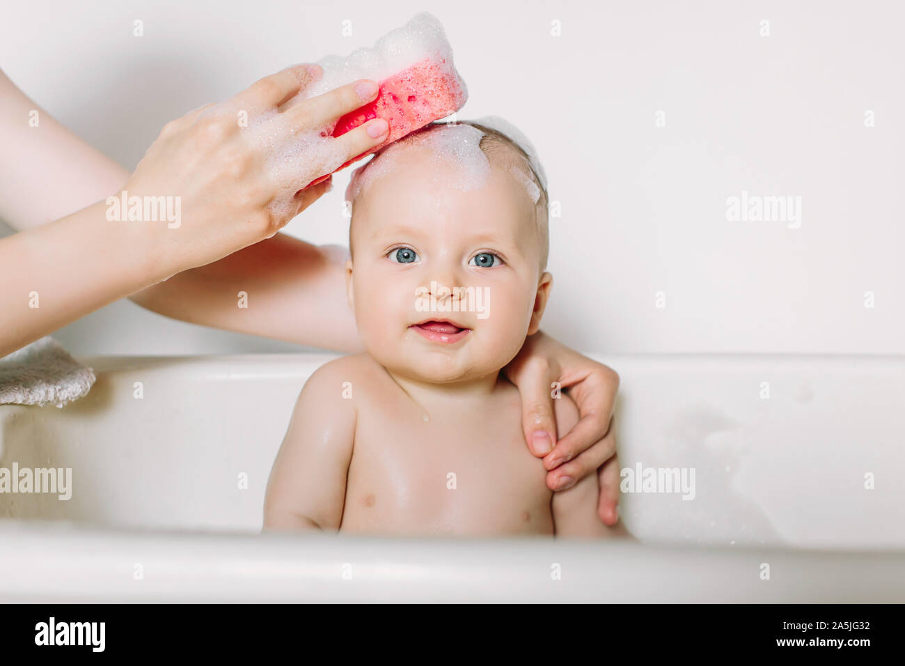 Happy laughing baby taking a bath playing with foam bubbles. Little