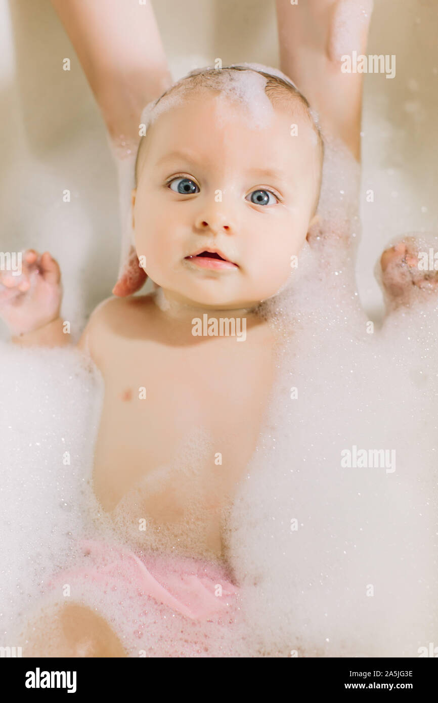 Happy laughing baby taking a bath playing with foam bubbles. Little