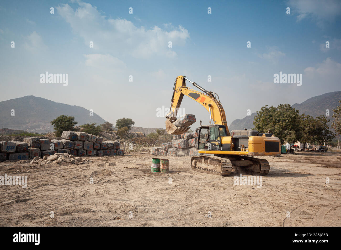 An excavator moves a rough cut granite block into a stockyard in Ongole, India Stock Photo