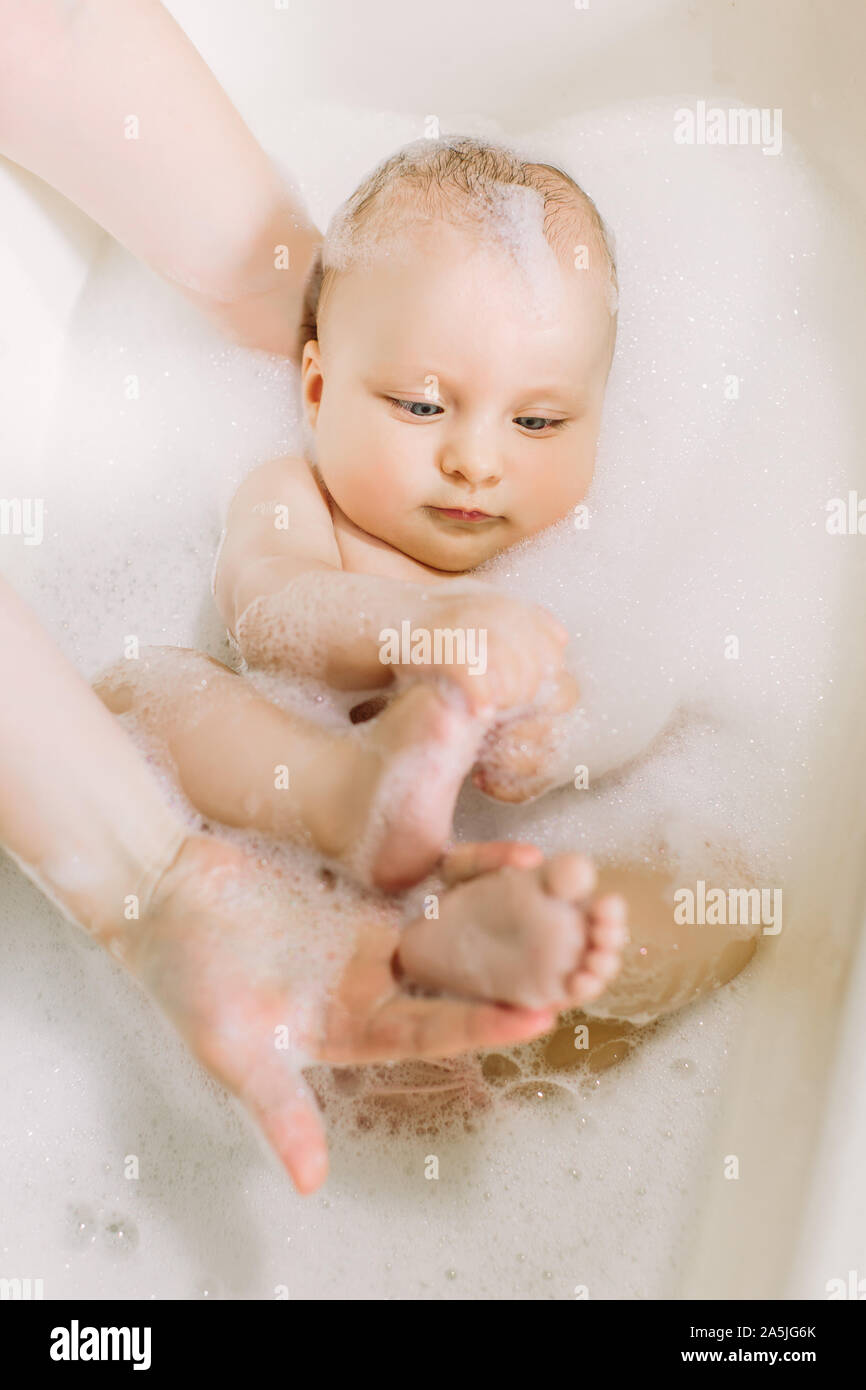 Happy laughing baby taking a bath playing with foam bubbles. Little