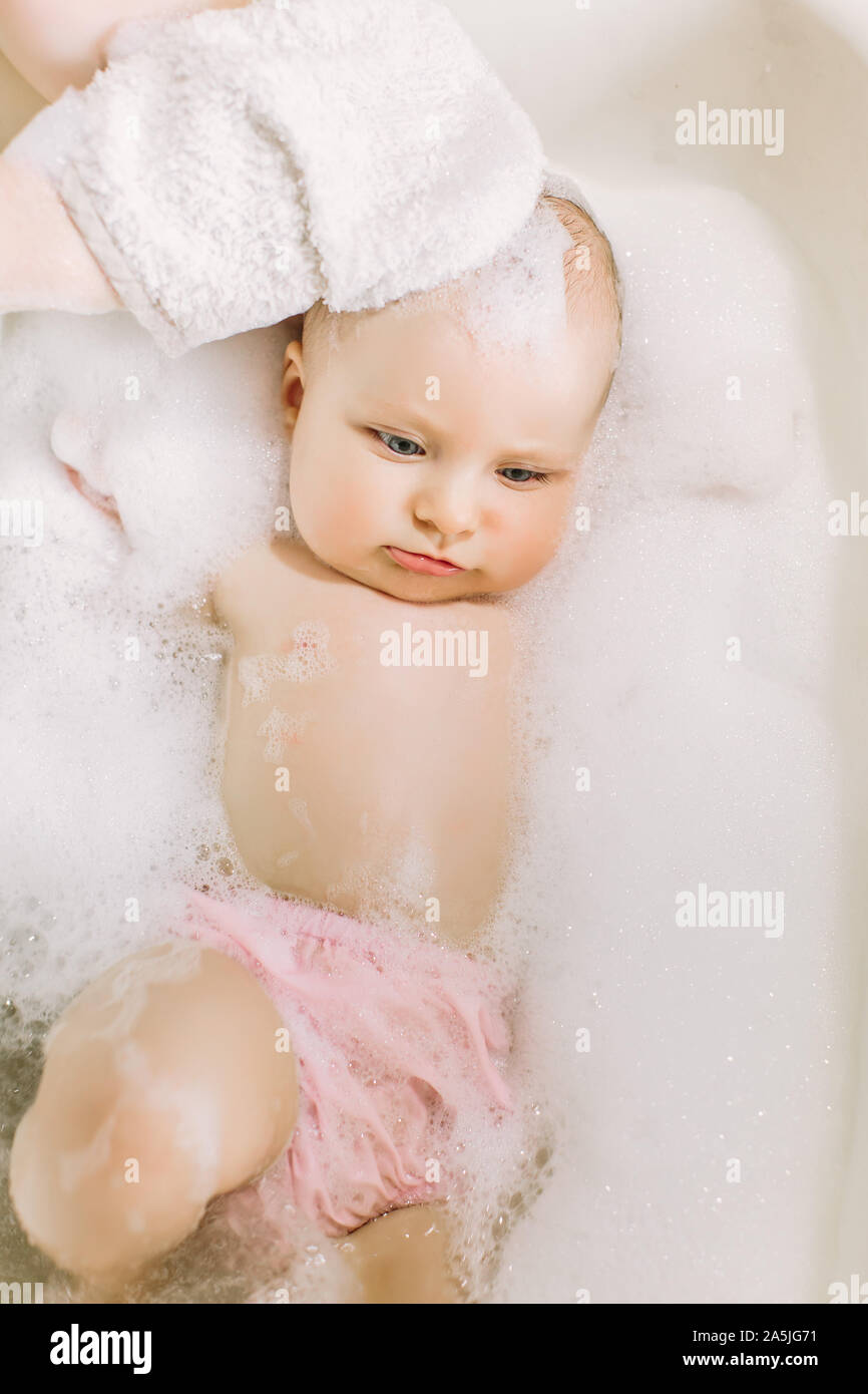 Happy laughing baby taking a bath playing with foam bubbles. Little