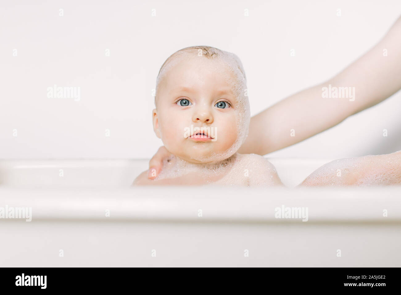Happy laughing baby taking a bath playing with foam bubbles. Little
