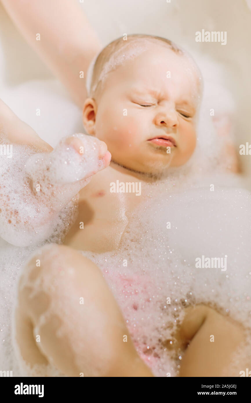 Happy laughing baby taking a bath playing with foam bubbles. Little