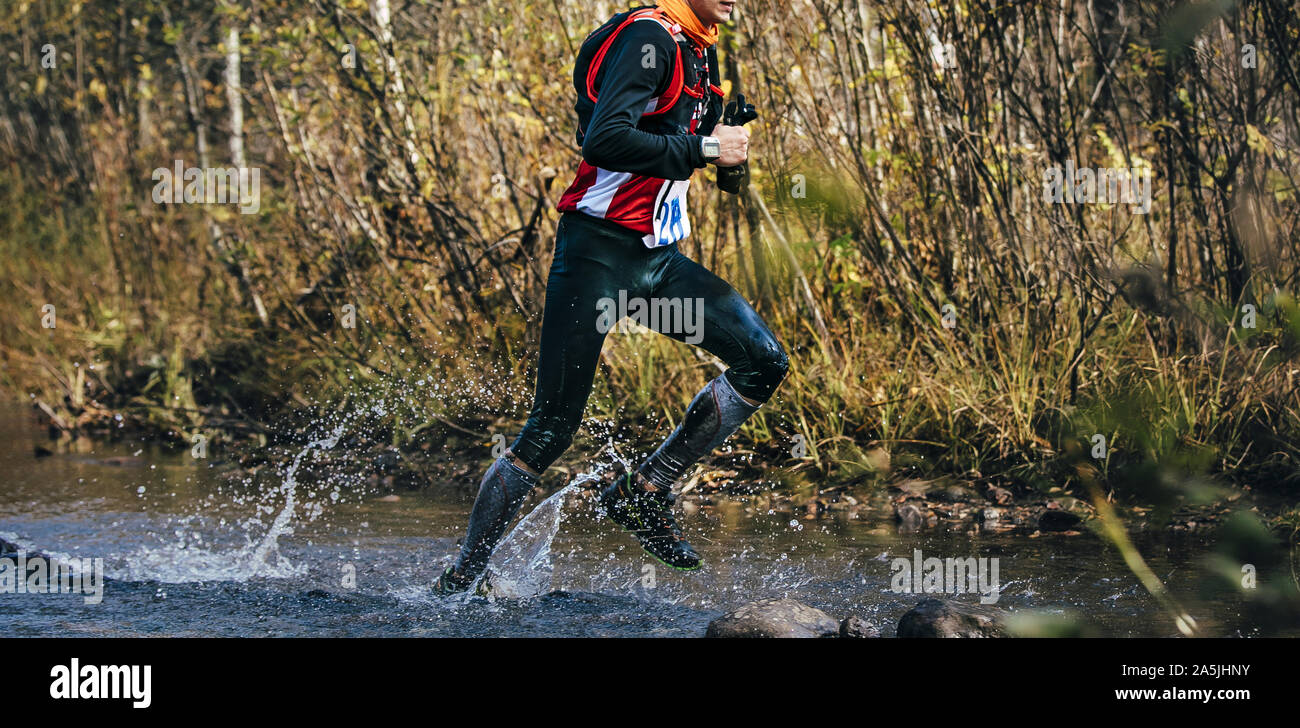 athlete runner with camelbak running fall marathon crossing river Stock Photo