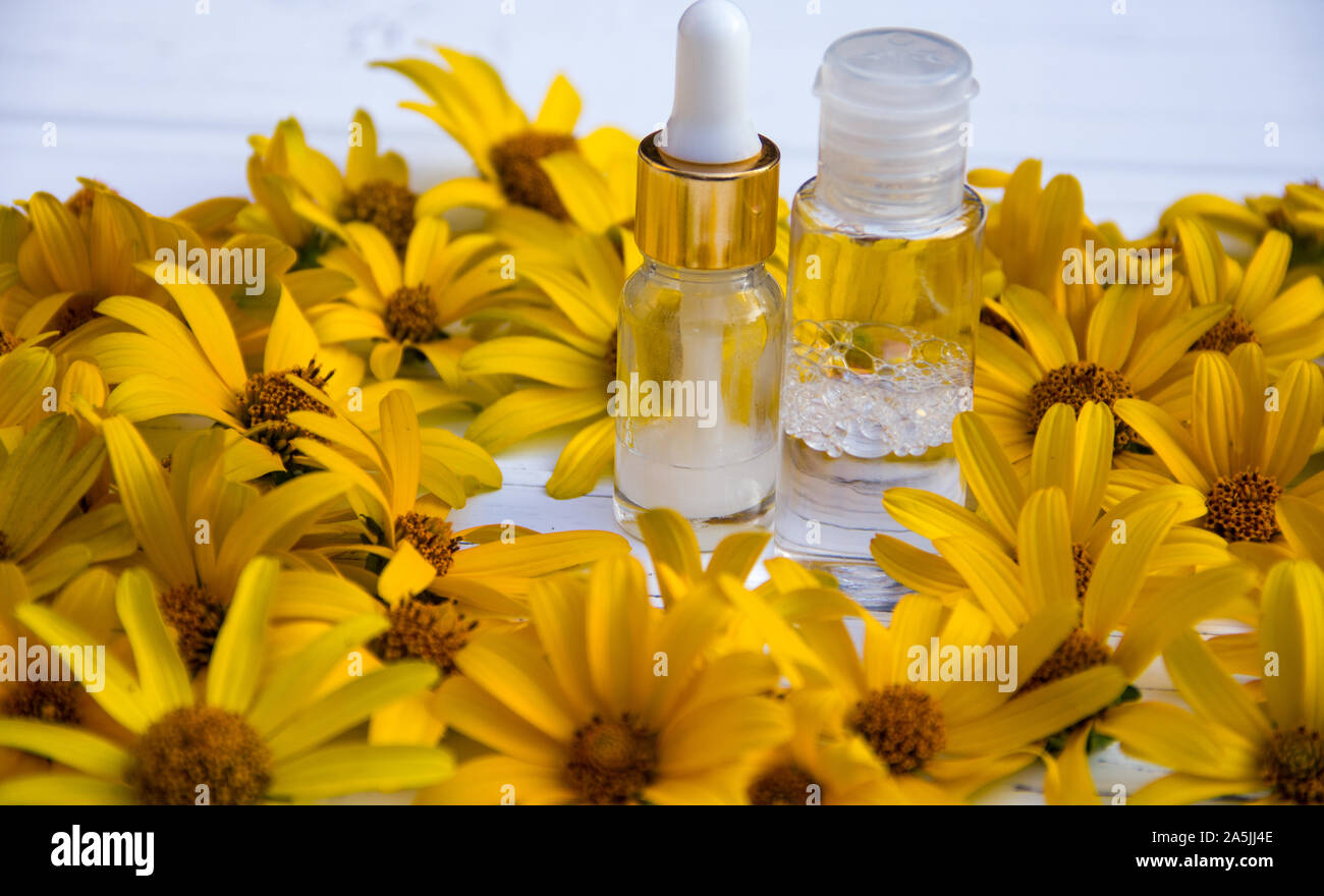 yellow flowers and white cosmetic cream in a bottle and tonic on a wooden light background Stock Photo