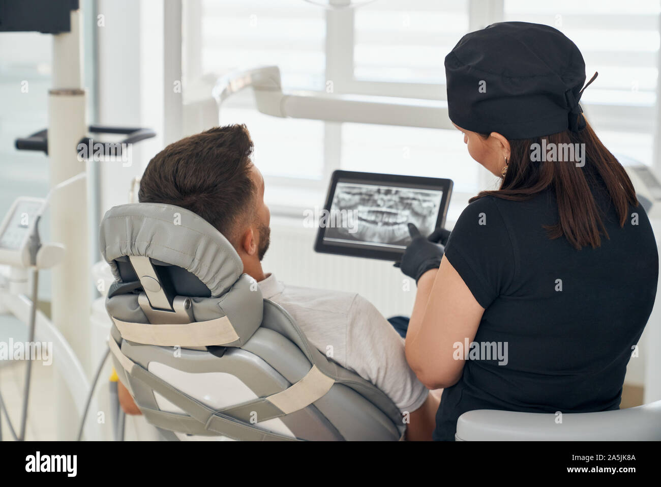 View from back of clever female dentist in uniform keeping tablet and