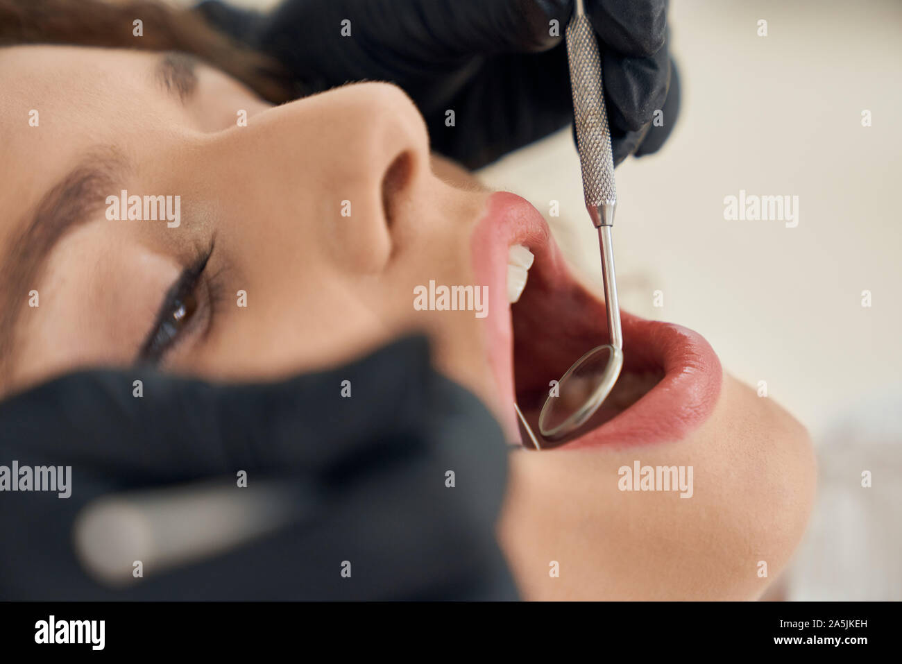 Closeup female face with opened mouth and hands of dentist keeping probe and mirror in clinic. Woman visiting dental office and curing teeth. Concept of treatment, care and health. Stock Photo