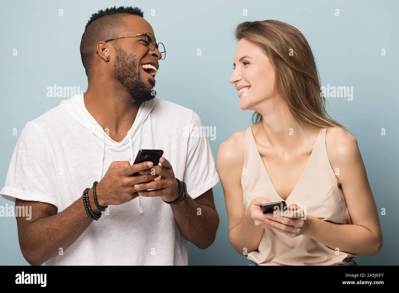 Happy multiethnic couple laugh using smartphones together Stock Photo