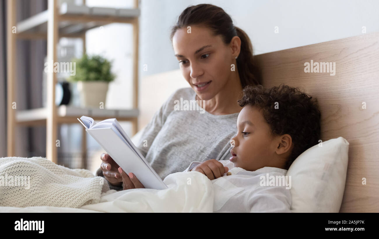 Caring mom reading book to little son in bed Stock Photo
