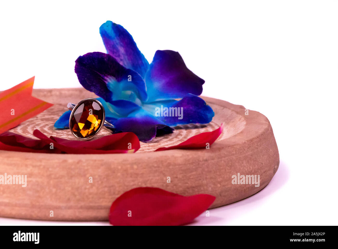 Ring gift concept. Amber stone ring with rose petals and blue orchid flowers on white background Stock Photo