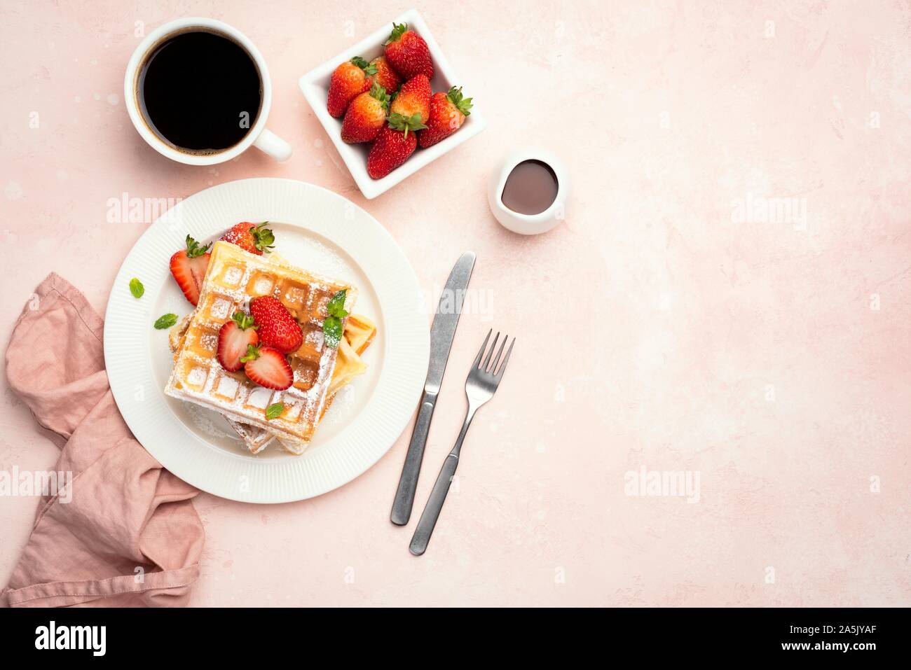 Belgian waffles with strawberries and cup of coffee on a pink background, table top view with copy space. Tasty sweet breakfast food Stock Photo