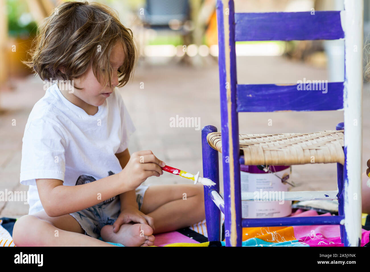 5 year old boy painting children's chair on porch with his sister Stock Photo