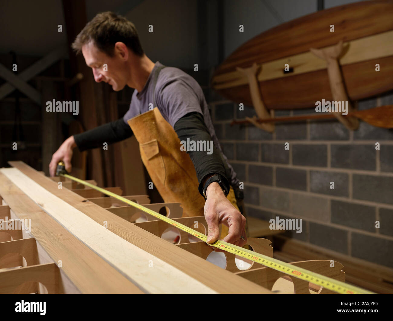 Man in workshop using expanding tape measure to make wooden paddleboard Stock Photo