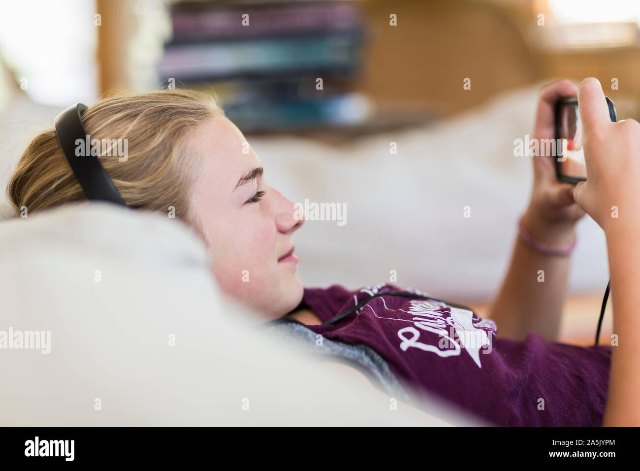 13 year old girl at home wearing headphones and looking at smart phone Stock Photo