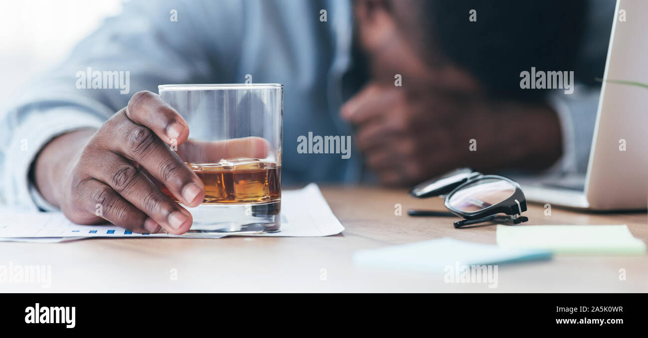 Drunk black employee sleeping at workplace, holding glass with alcohol Stock Photo
