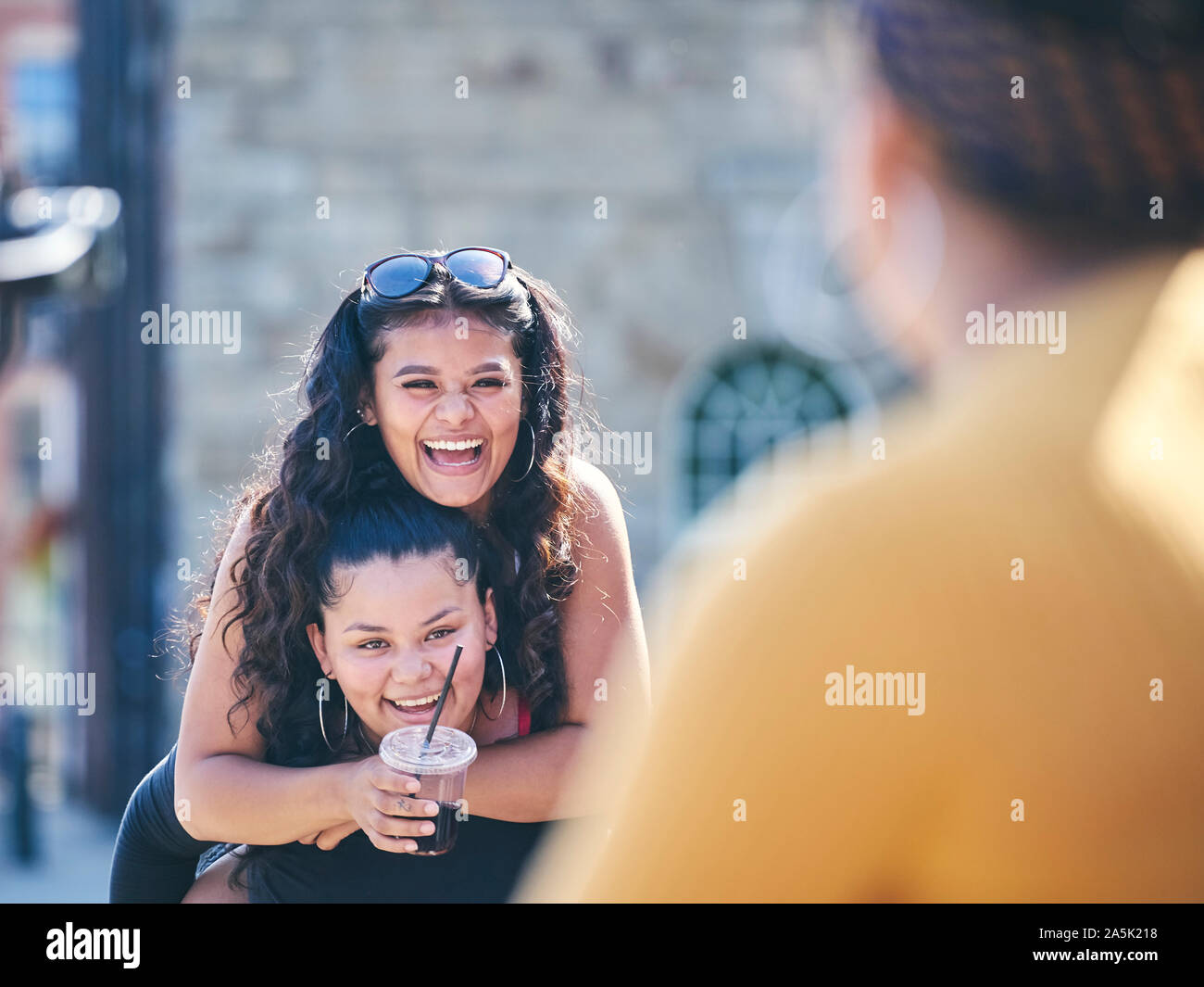 Young woman getting piggy back from teenage sister, over shoulder view Stock Photo
