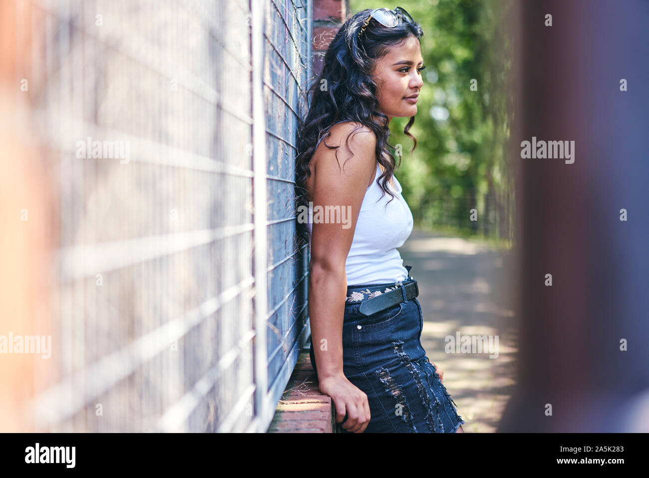 Young woman with long black hair leaning against wall Stock Photo - Alamy