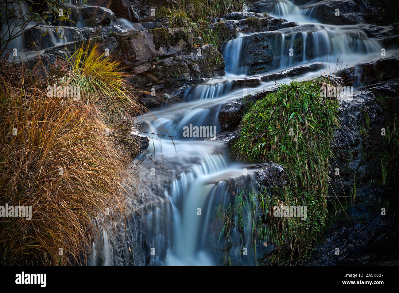 Waterfall cascading over rocks with grasses Stock Photo