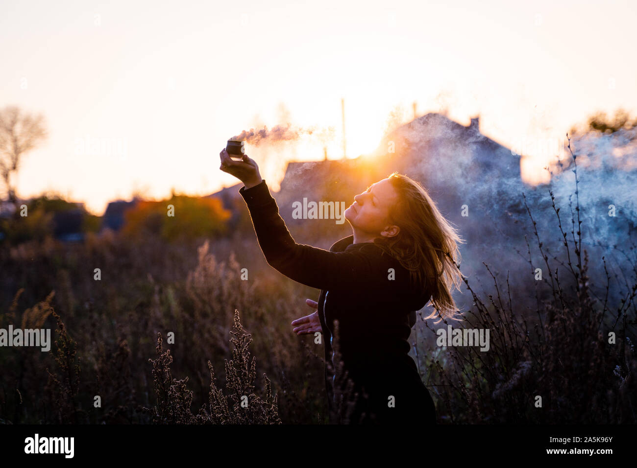 woman with long hair holds a smoking bowl in her hand, profile portrait at sunset. allegory of magic. Stock Photo