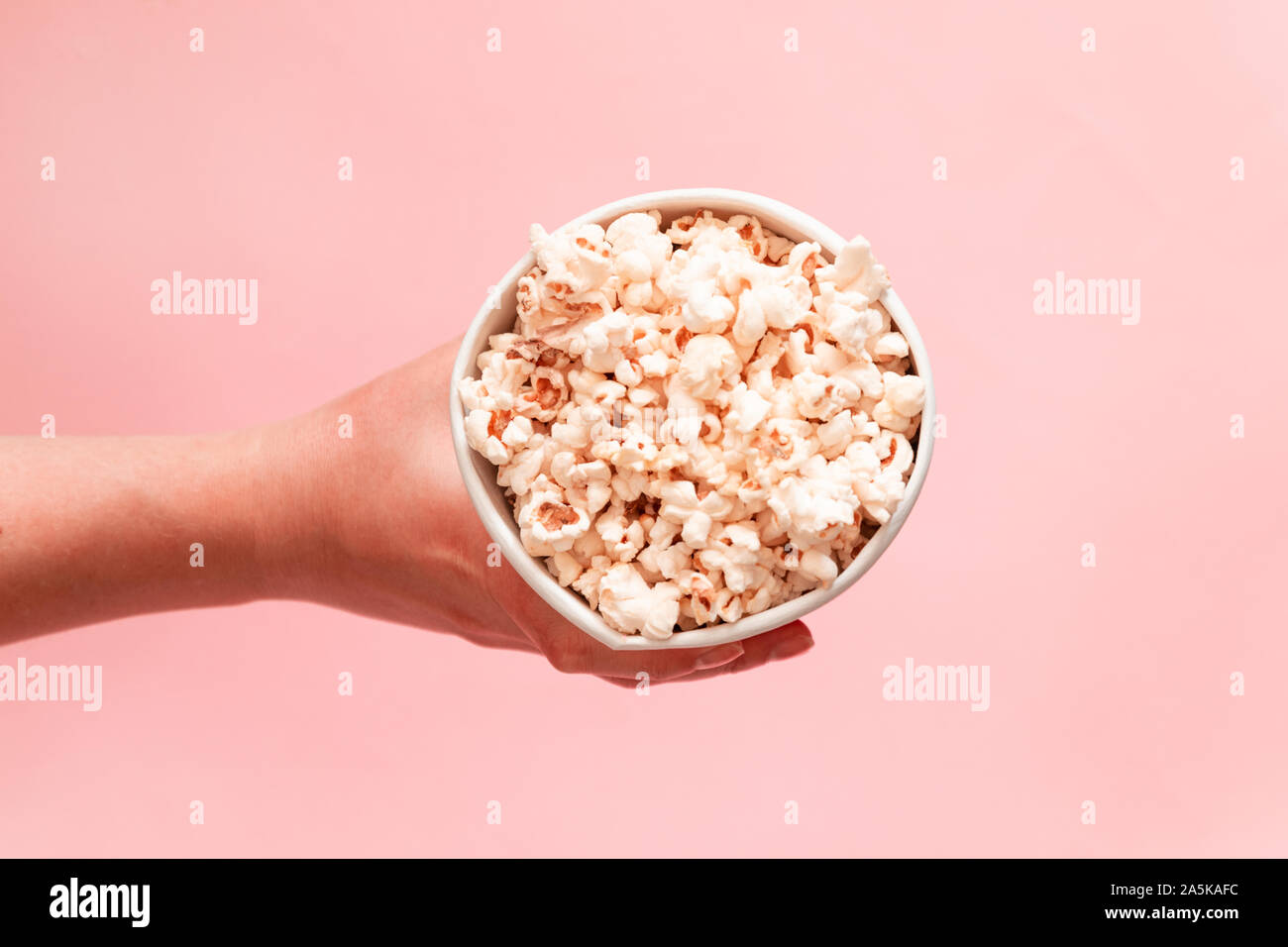 Food composition of hand holding popcorn in bucket on pink background top view copy space Stock Photo