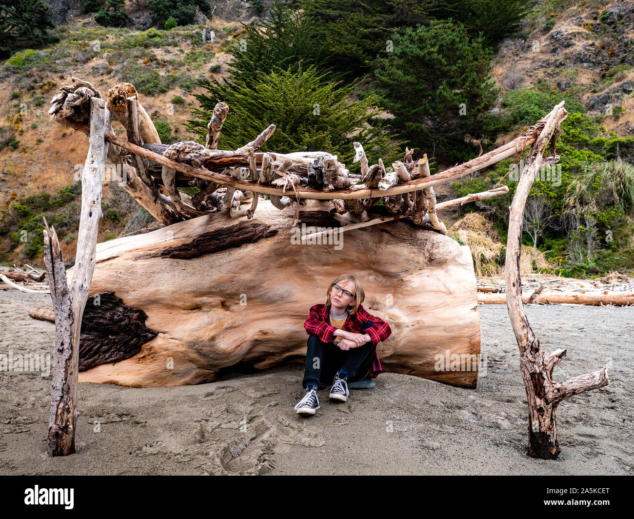 Tween boy sitting in driftwood structure at the beach Stock Photo