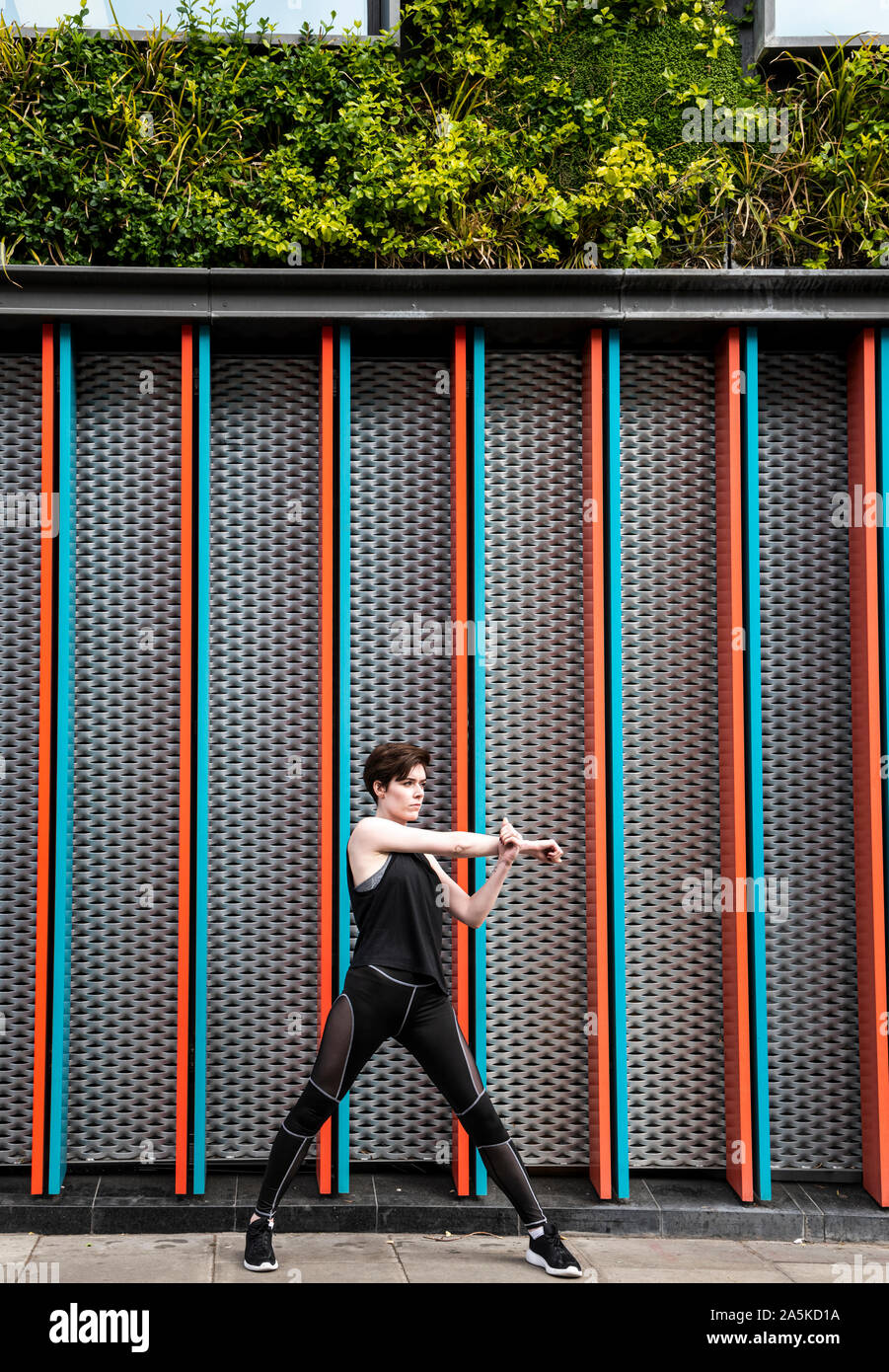Young woman practicing yoga on city sidewalk, full length Stock Photo