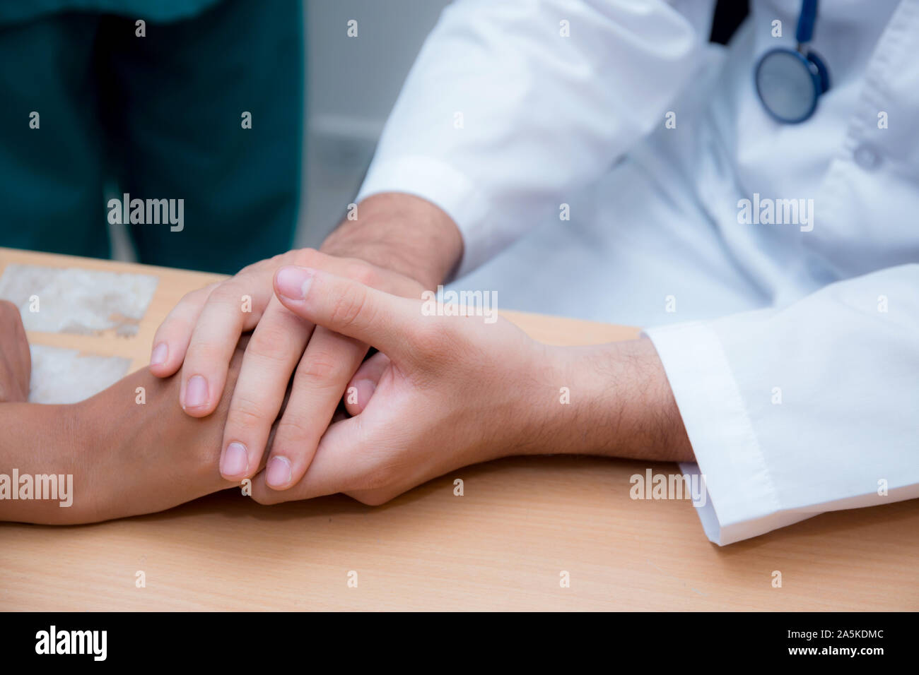 Friendly male doctor hand holding patient hand sitting at the desk for encouragement - empathy - cheering and support while medical examination. Stock Photo